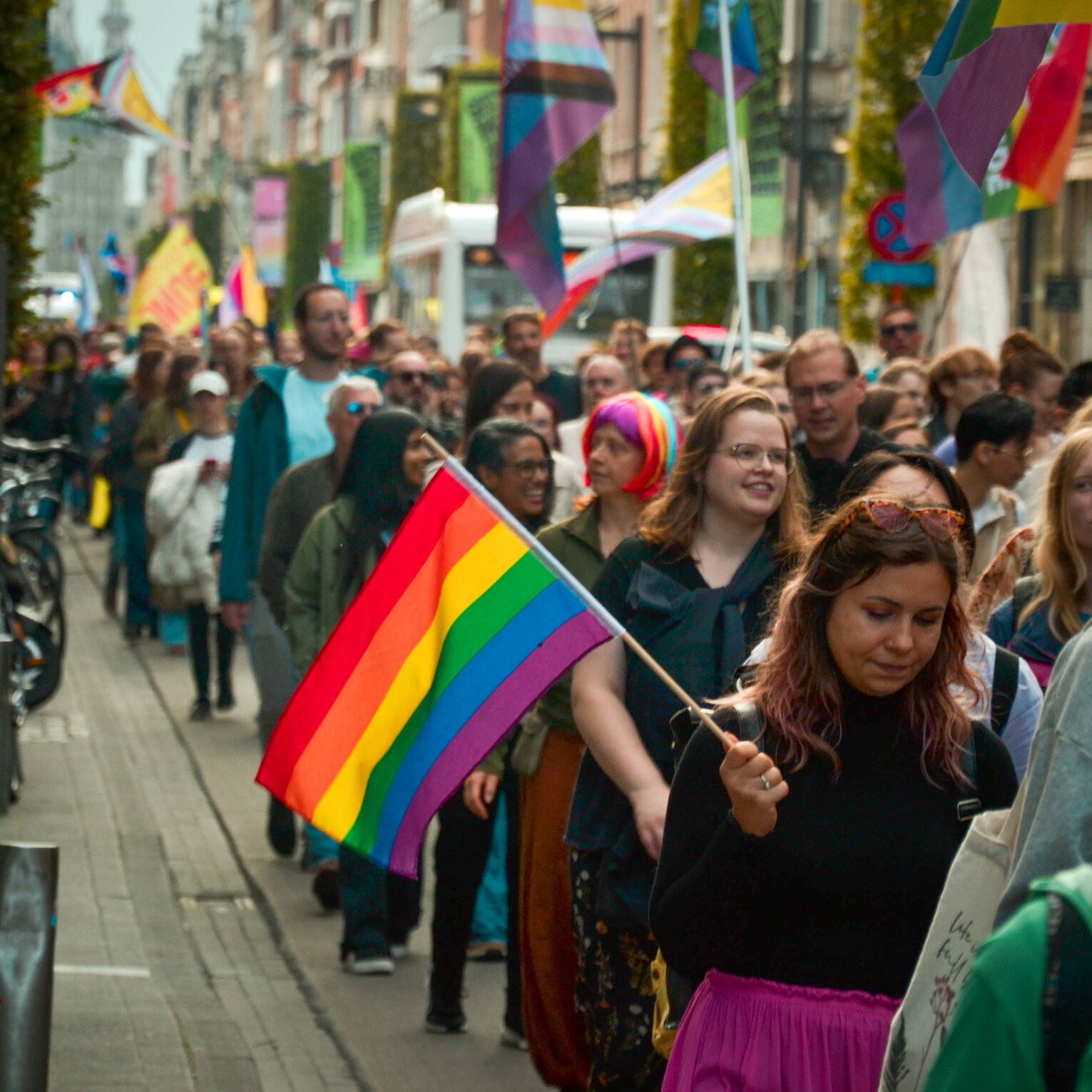 Walking with a rainbow flag under the flags hung along the street. Leuven Pride 2025, photo: Cato Van Den Kerckhove