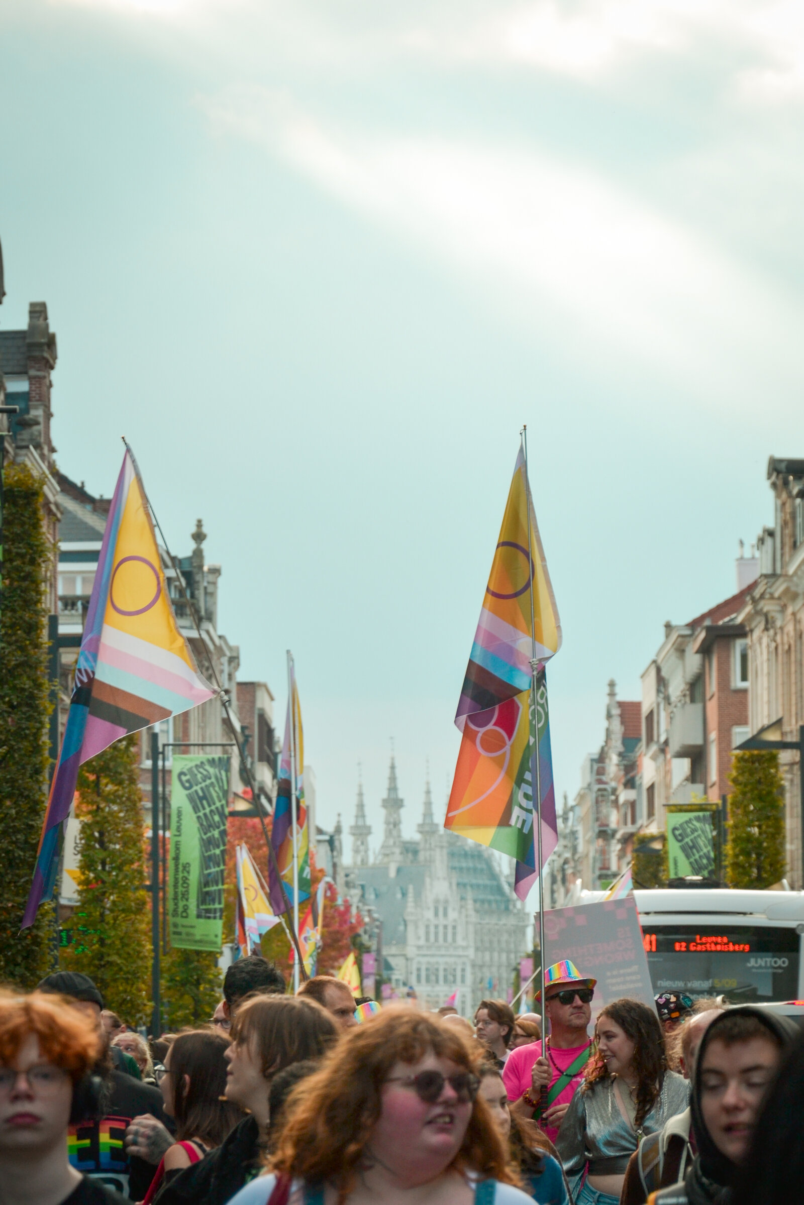 Progress Pride flags on the lamp posts along the route, the towers of the old centre at the end of the street. Leuven Pride 2025, photo: Cato Van Den Kerckhove
