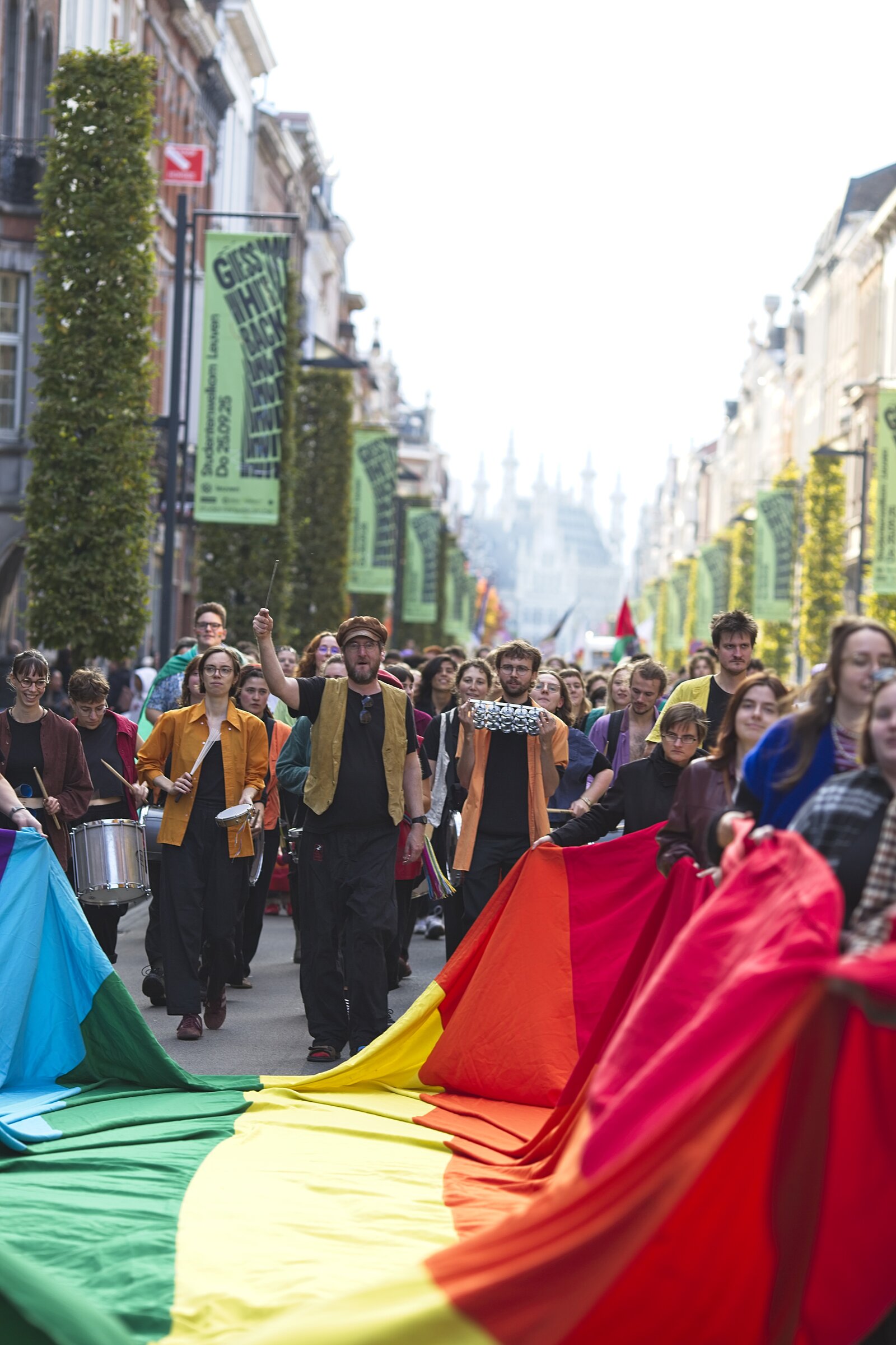 The walk fills the width of the street behind the flag. Leuven Pride 2025, photo: Jeroen Van Nieuwenhove