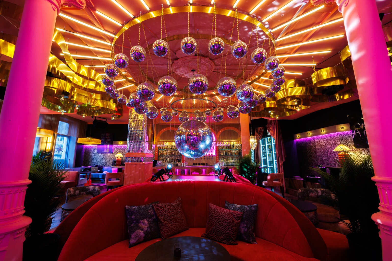 The centre of the room: a ring of disco balls around one large mirror ball between two pink columns, above a round red velvet sofa