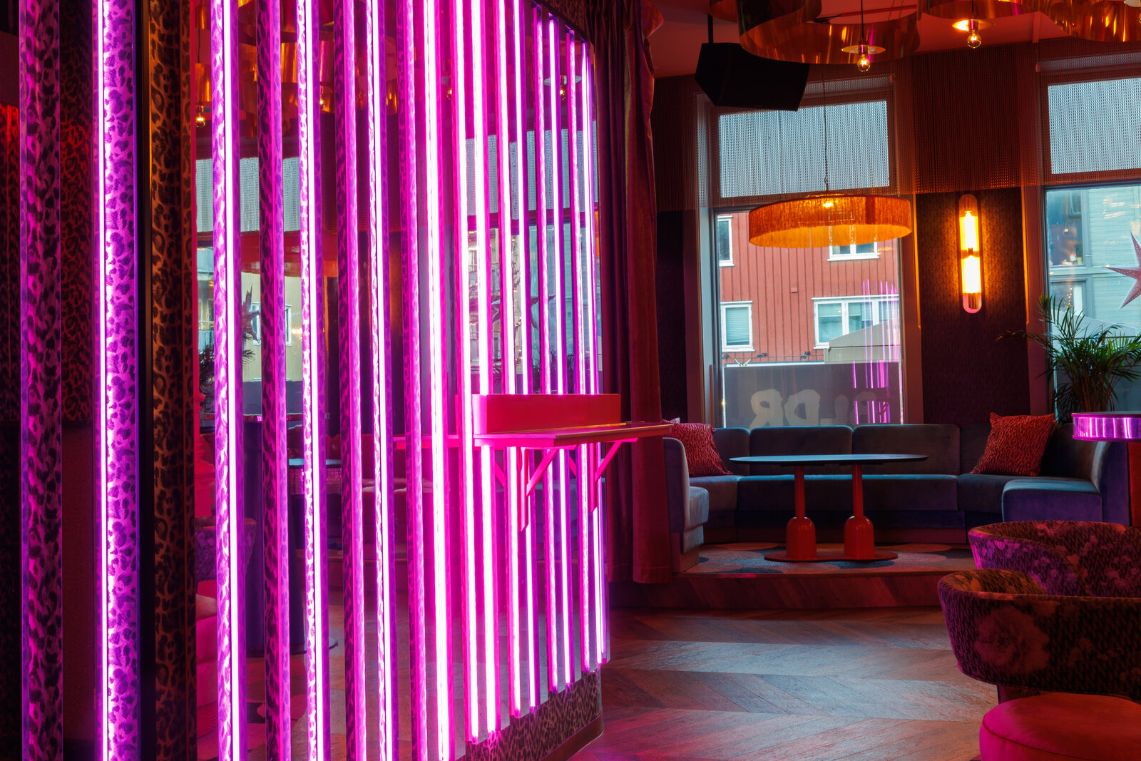 A screen of pink neon tubes with a small ledge for drinks, and a velvet booth by the window behind it