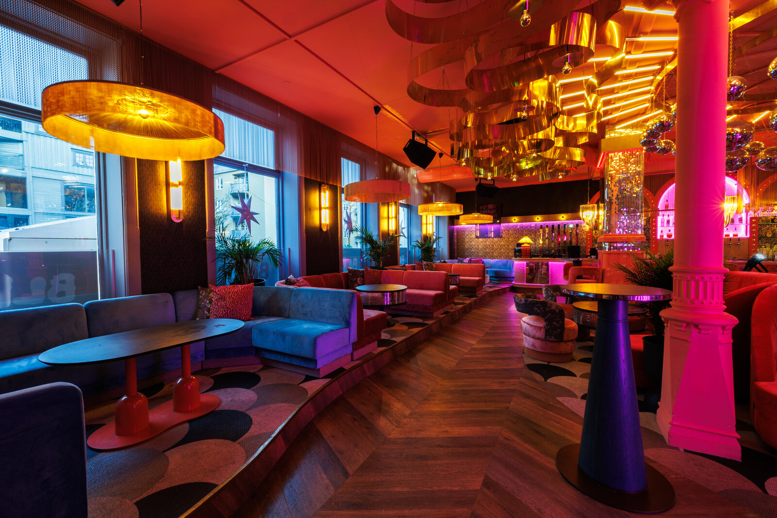 The long room along the street windows, with velvet booths on a raised floor, gold ribbon lights overhead and the bar at the far end