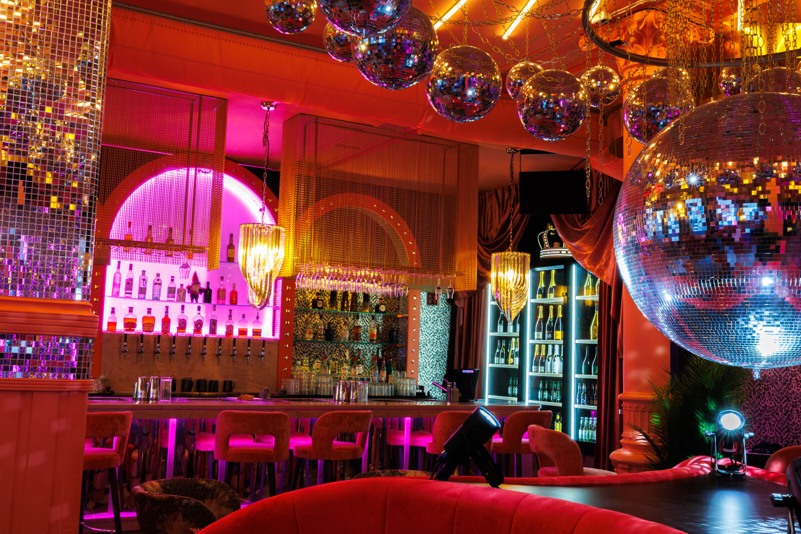 The bar seen past a huge mirror ball, with smaller disco balls overhead, a pink-lit back bar and velvet stools at the counter