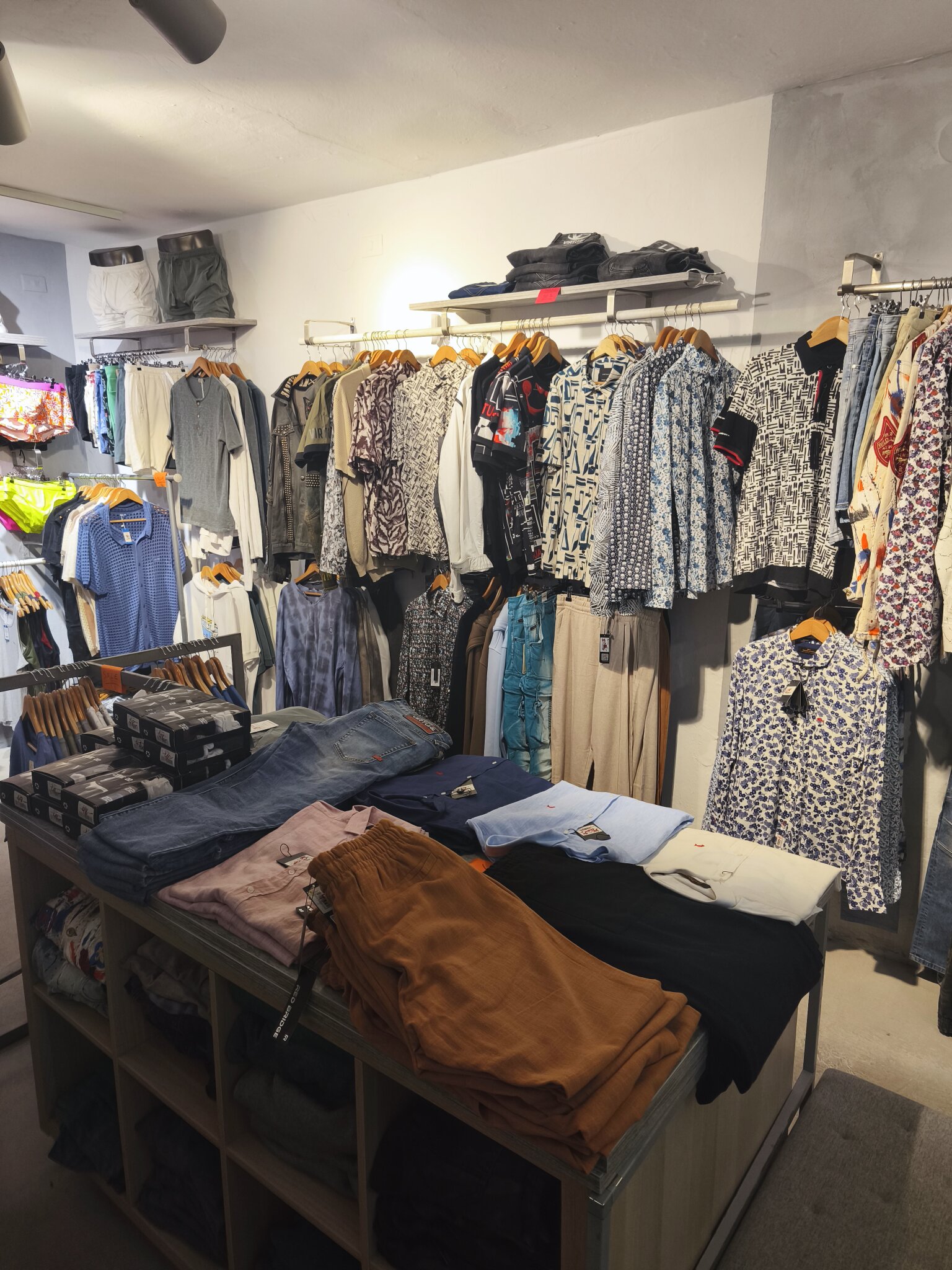 Printed short-sleeved shirts along the back wall, with trousers and folded shirts on the table below.