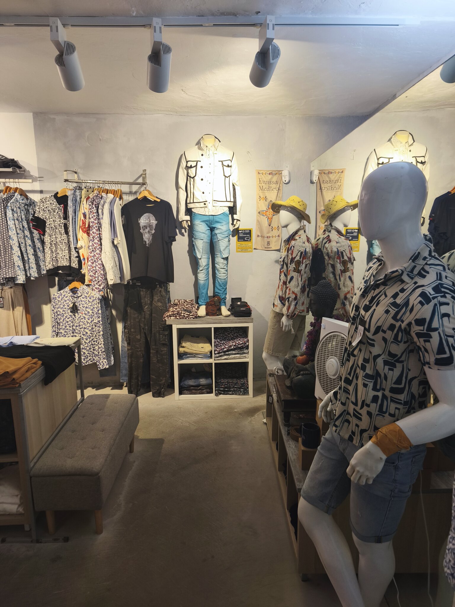 Mannequins at the back of the shop by the mirror, a denim jacket and jeans on display beside the printed shirts.