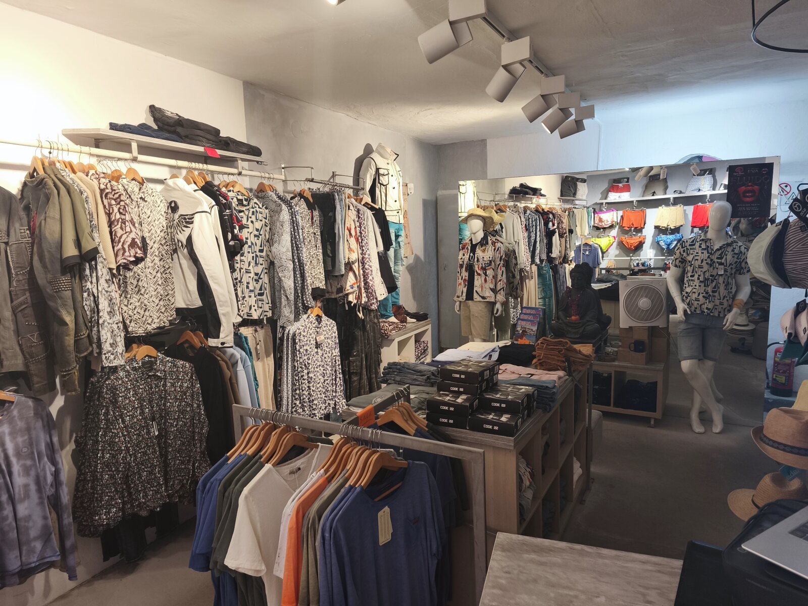 The shop floor seen from the door, patterned shirts on the wall rails and folded stock on the central table.