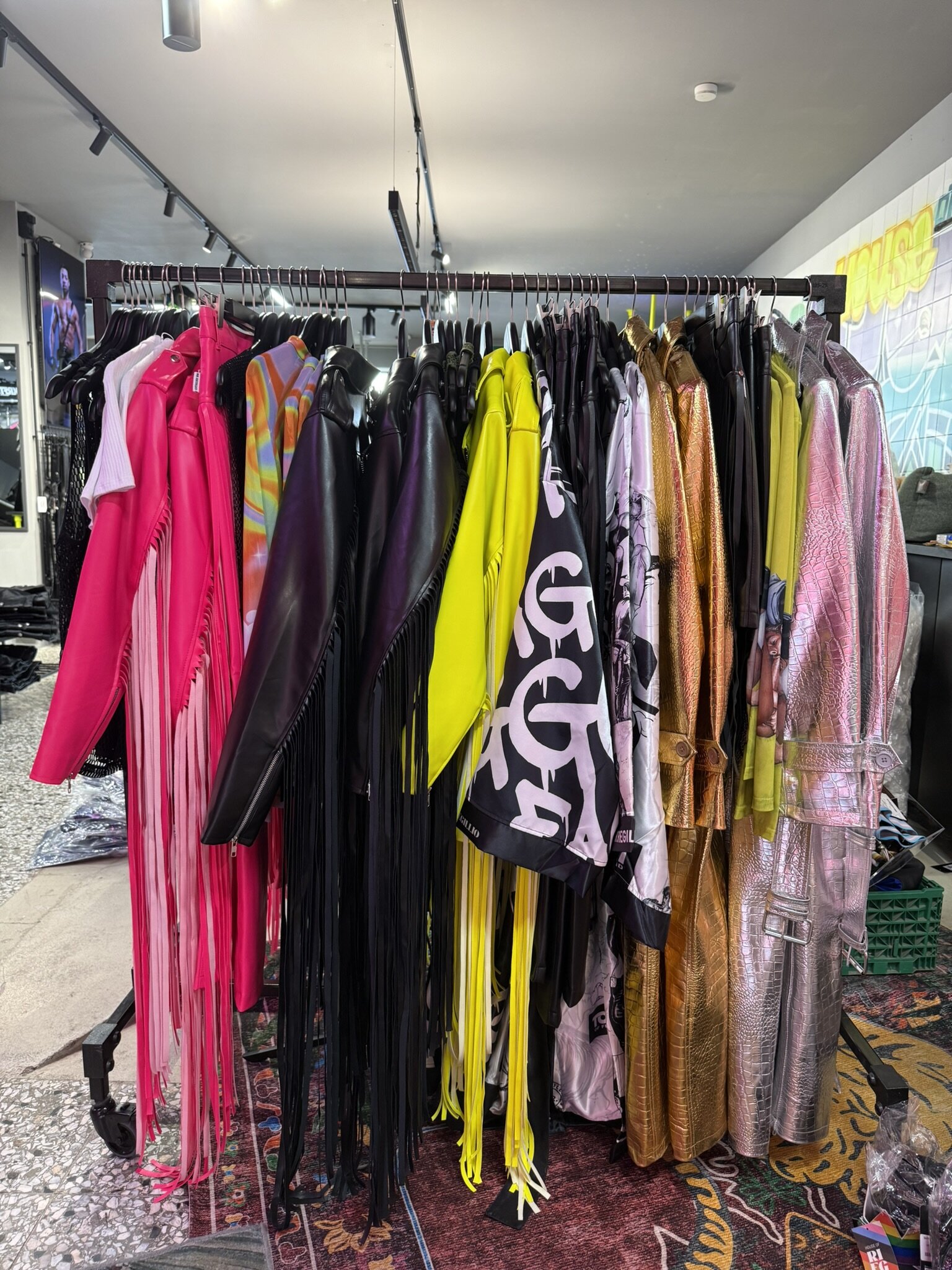 Clothes rail with fringed jackets in pink, black and yellow, printed shirts and metallic gold and silver coats.