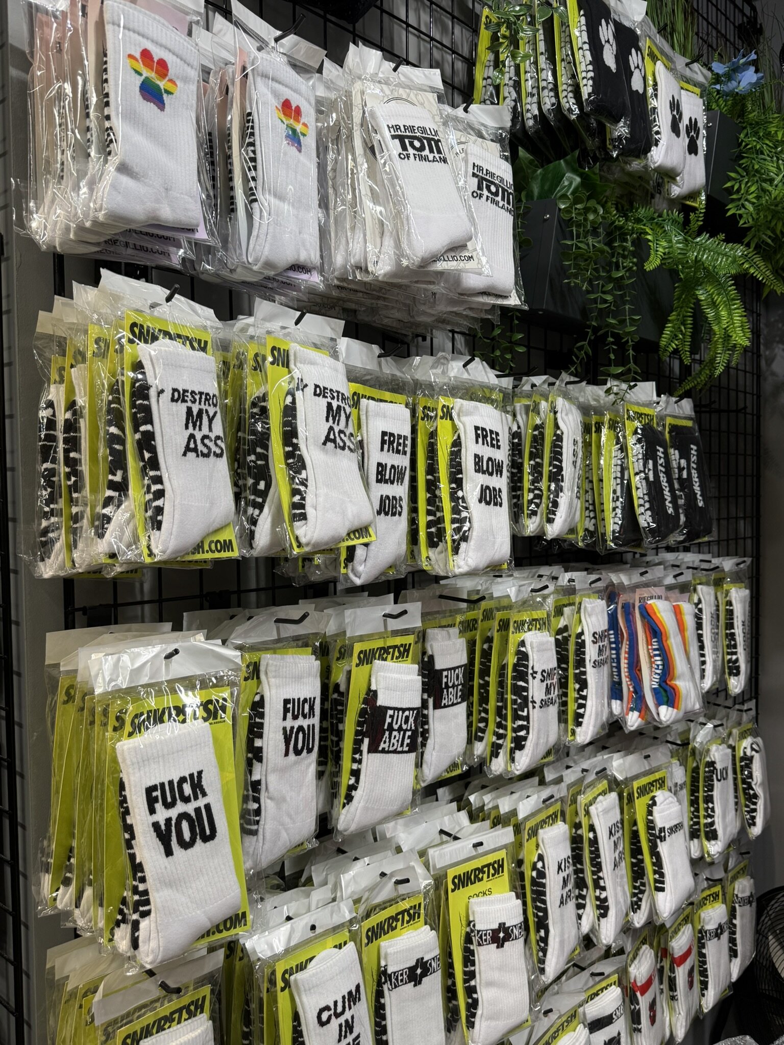 Wall of packaged socks with slogans and paw prints, some in rainbow colours, hung on a black grid.