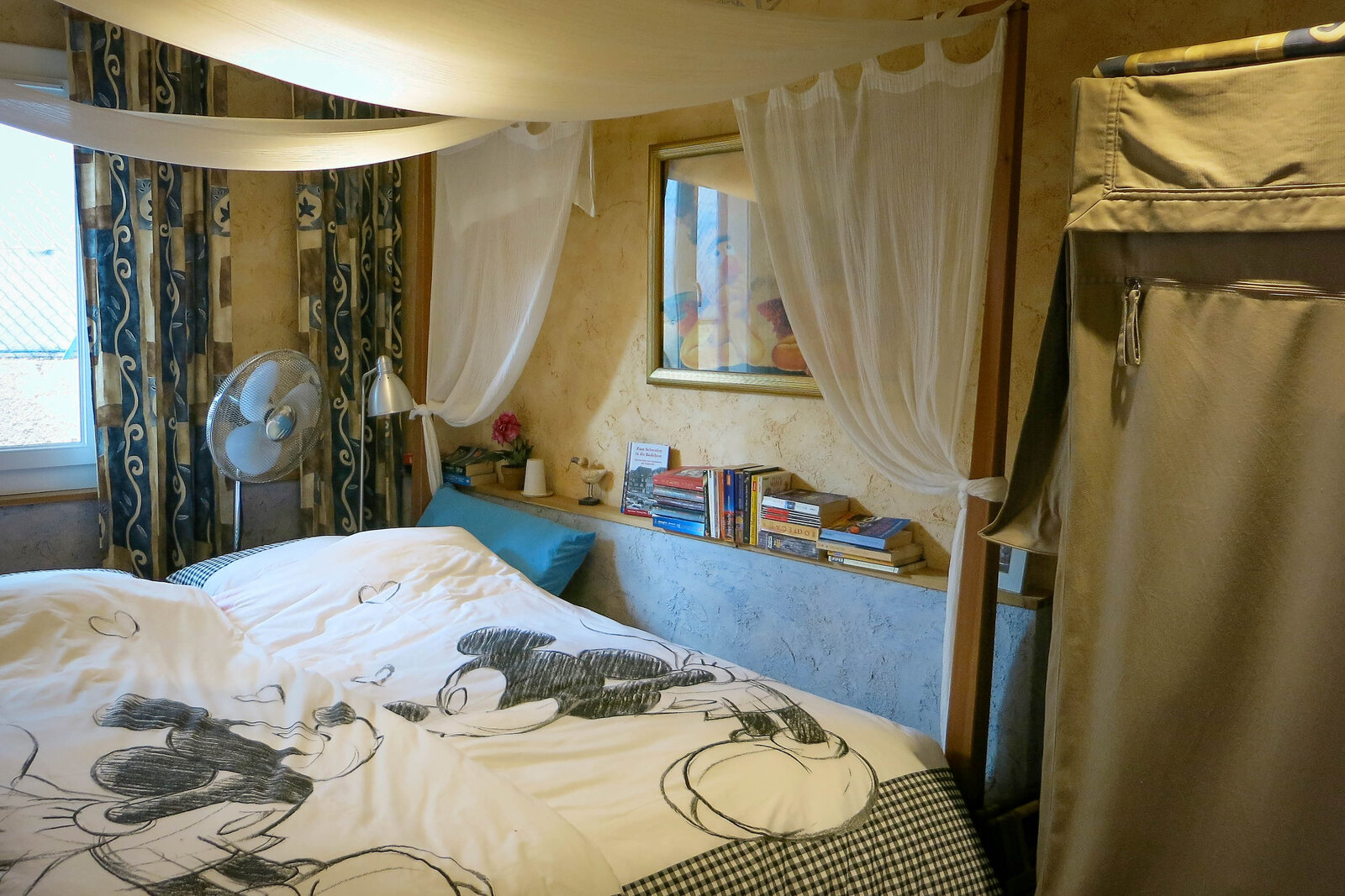 The double room, with white voile draped over the bed and a shelf of books