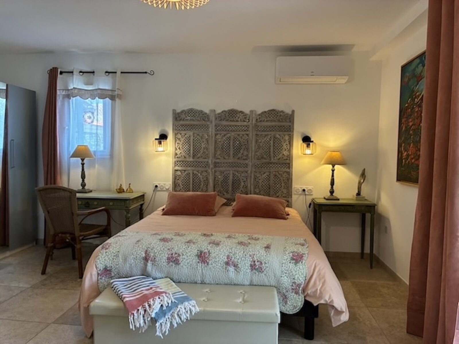A bedroom with a carved wooden folding screen behind the bed and blush pink bedding.