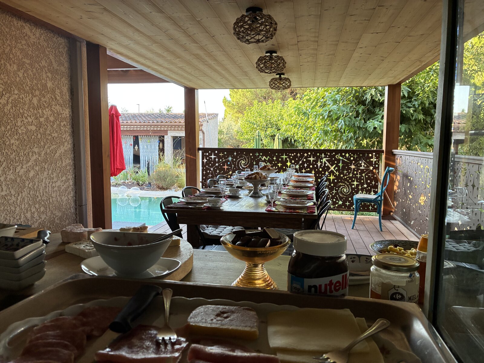 Breakfast laid on the covered terrace table overlooking the pool, with cold cuts, cheese and spreads on the counter in front.