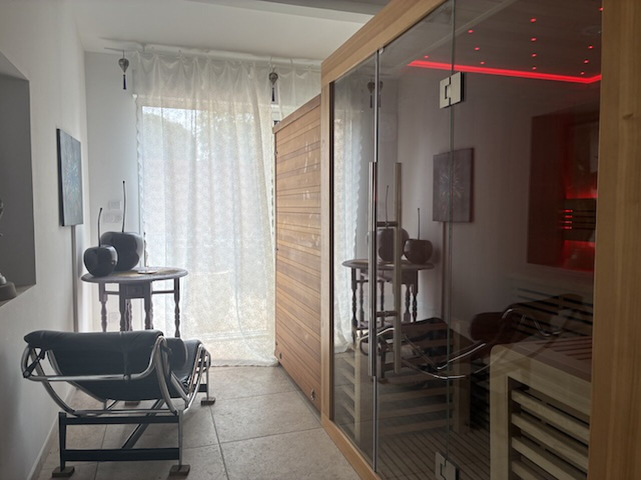The infrared sauna cabin lit red, next to a small relaxation corner by the terrace door.