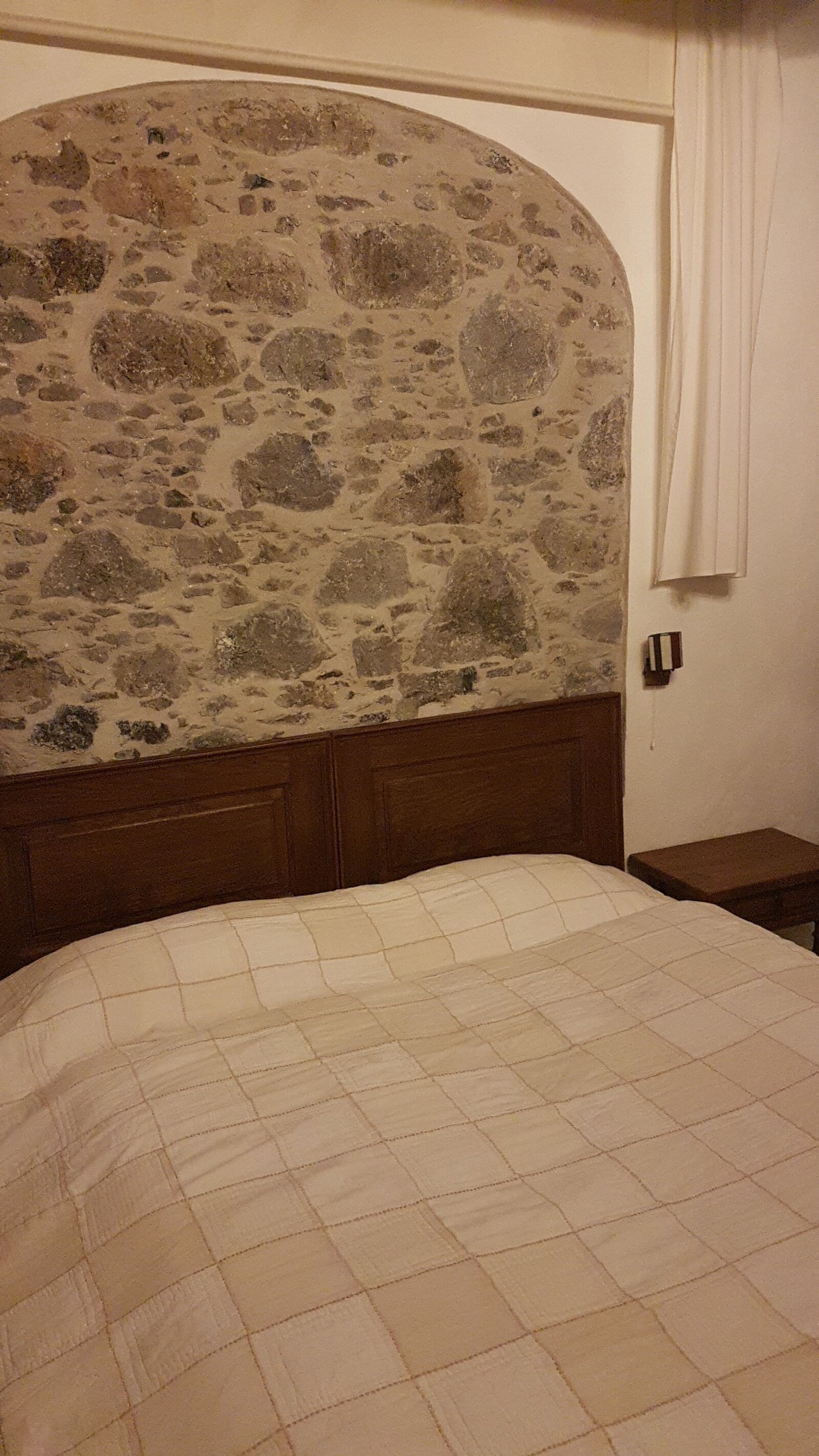 A double bed under the arched stone wall, with a carved wooden headboard
