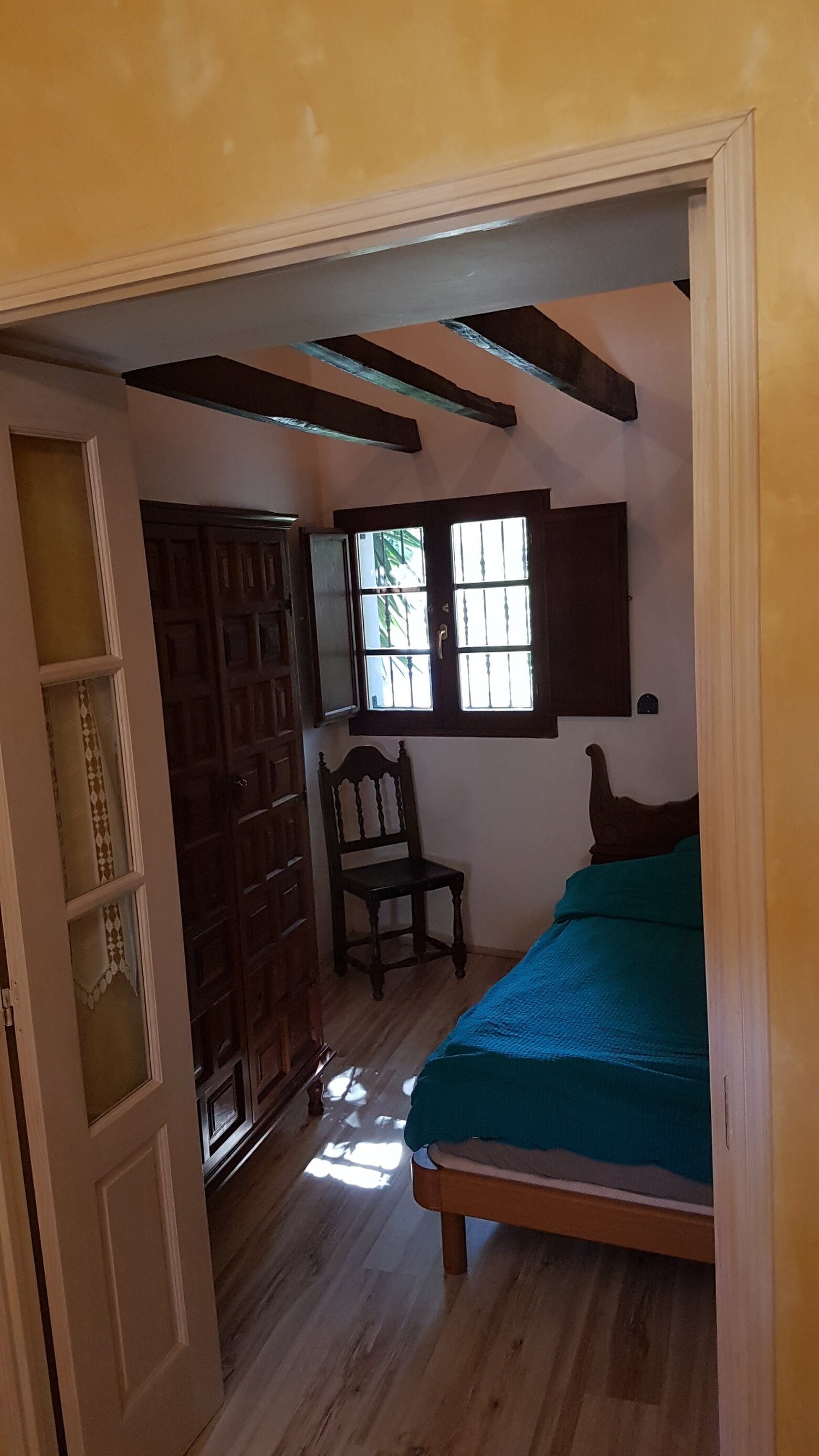A double bedroom with dark ceiling beams, an old Canarian wardrobe and wooden shutters