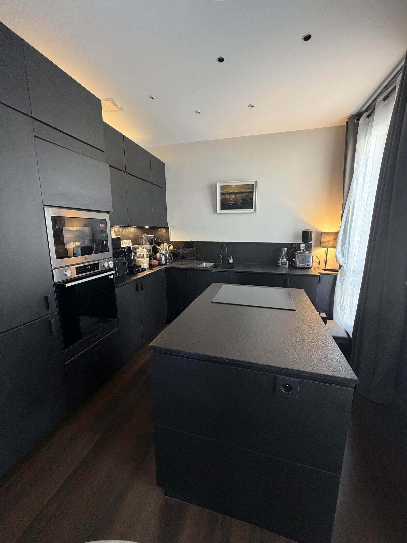 Kitchen with matt black cabinets, a built-in oven and microwave, and a black island in the middle.