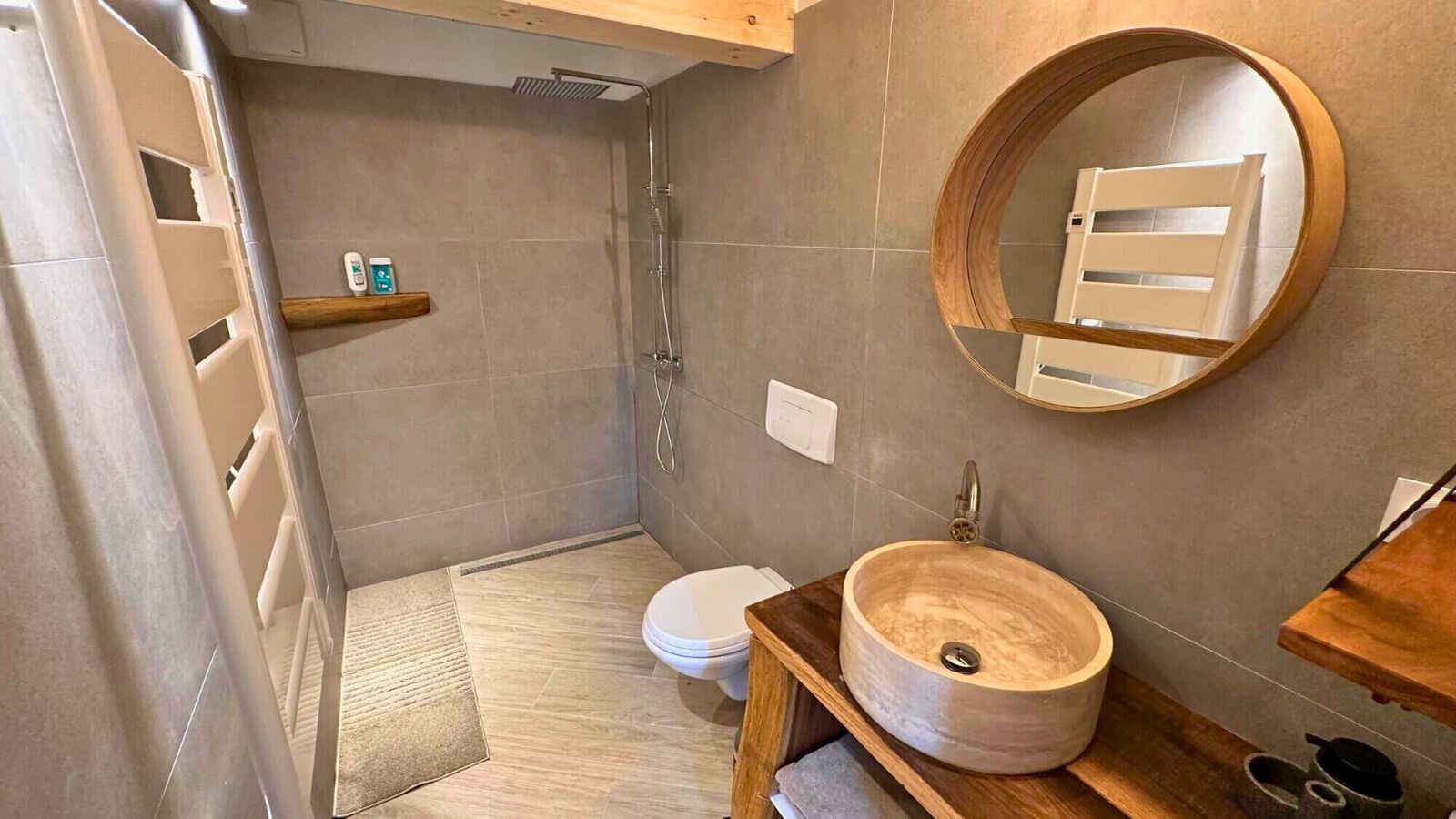 Shower room with a walk-in rain shower, a wall-hung toilet, a stone vessel basin on a wooden stand and a round mirror.