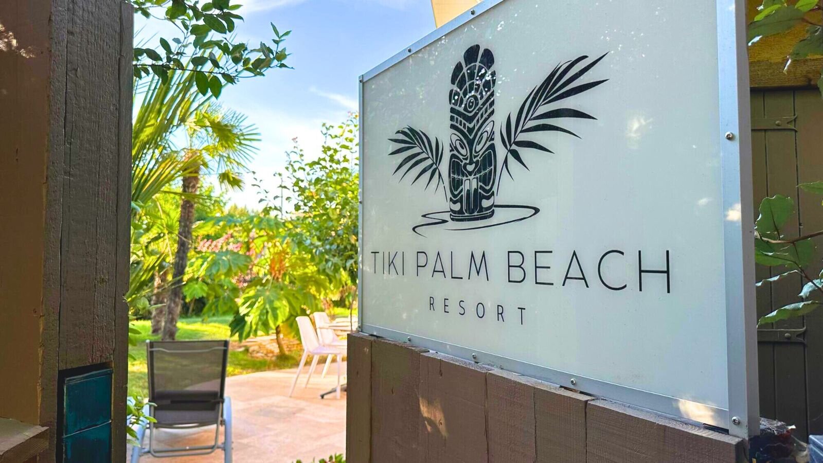 The resort's sign with a tiki mask and palm leaves at the entrance, the garden behind.