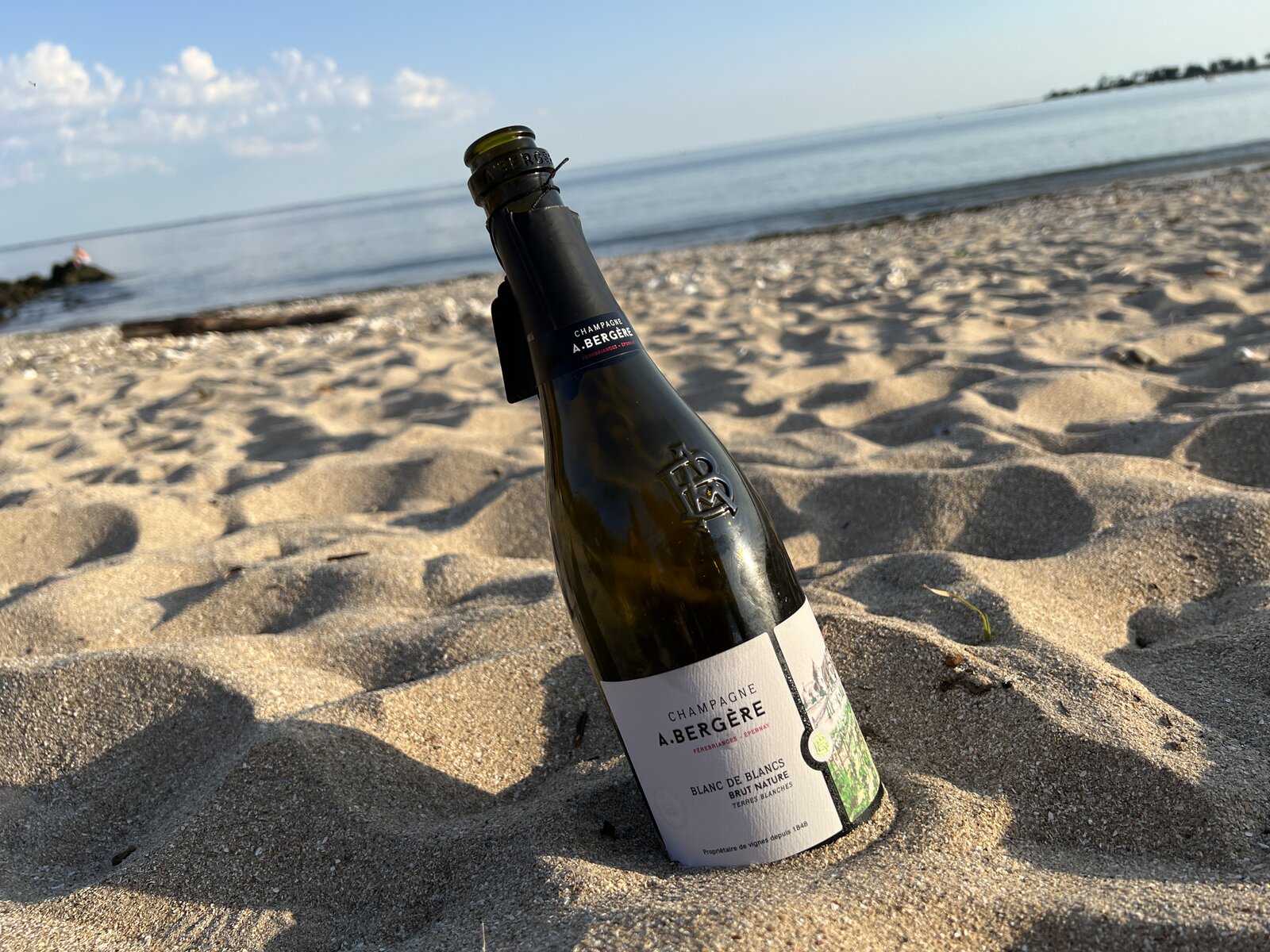 A bottle of Champagne in the sand on the beach at sunset.