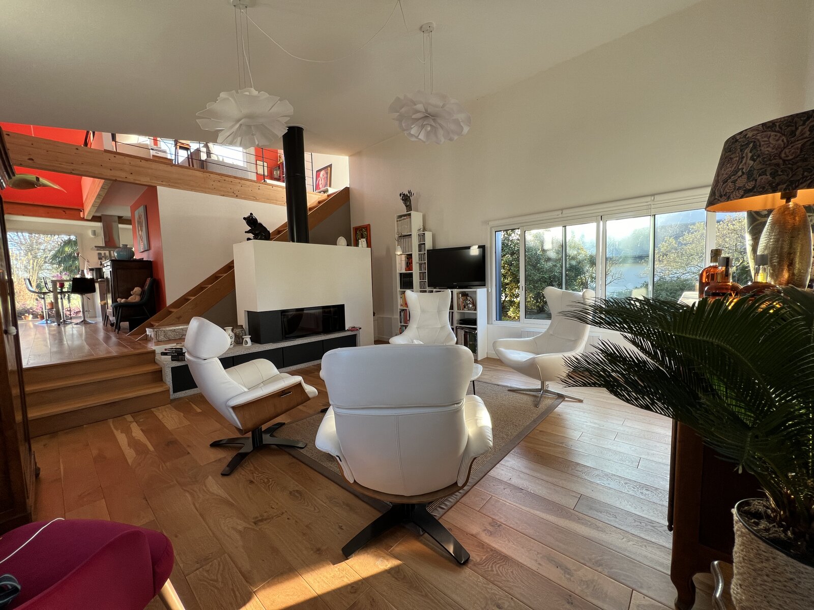 The bright living room with white leather swivel chairs and a wood-burning stove.