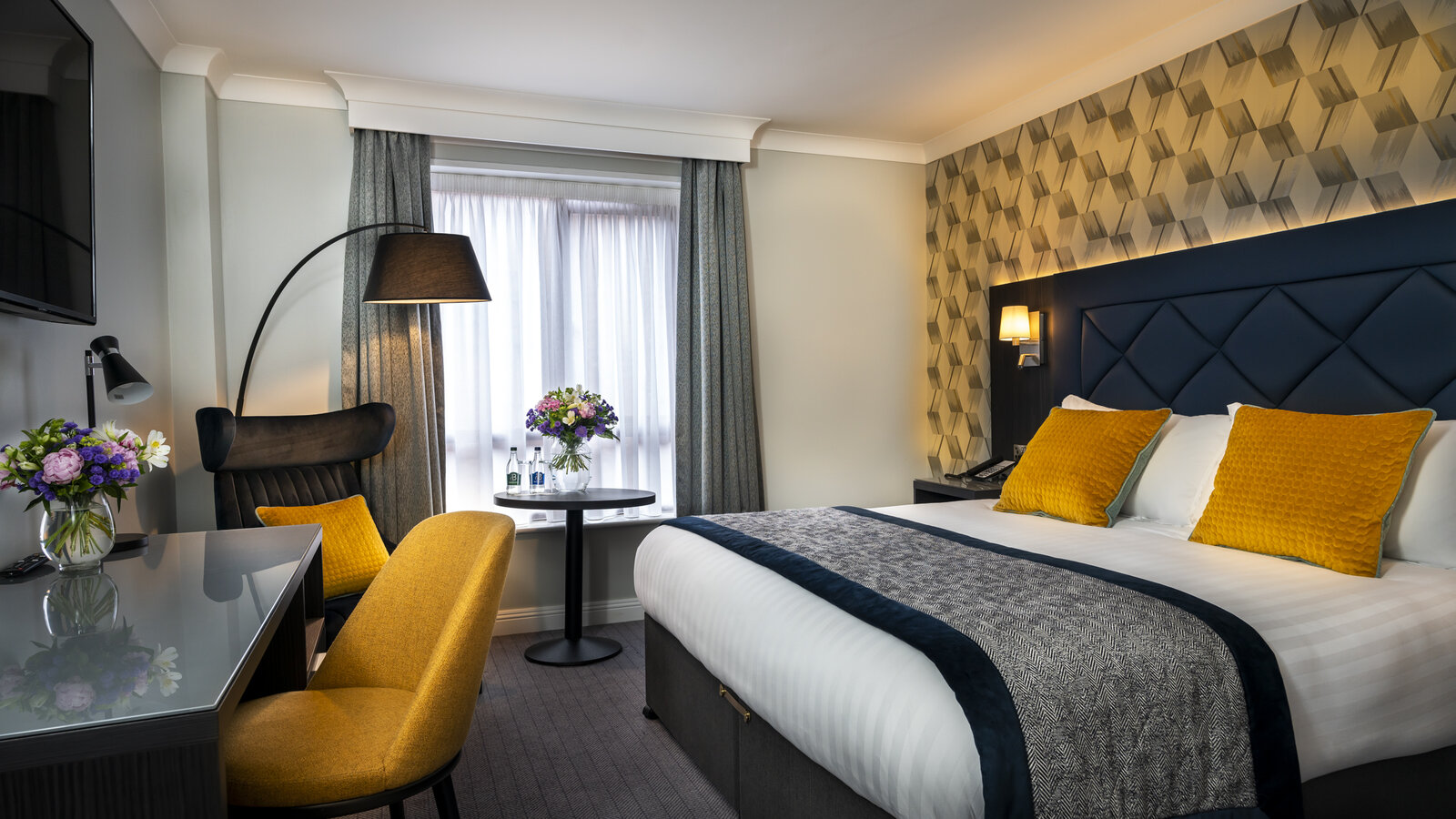 Double room with a navy upholstered headboard and a small seating area by the window.