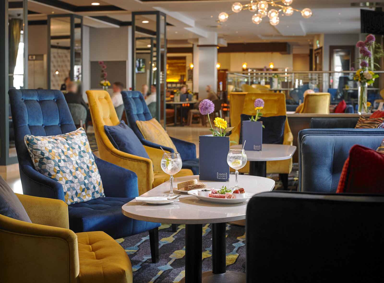 Lounge area with blue and mustard armchairs around small tables.