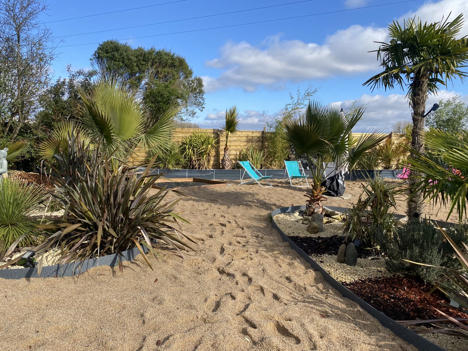 Sandy garden path with palm trees and deck chairs.