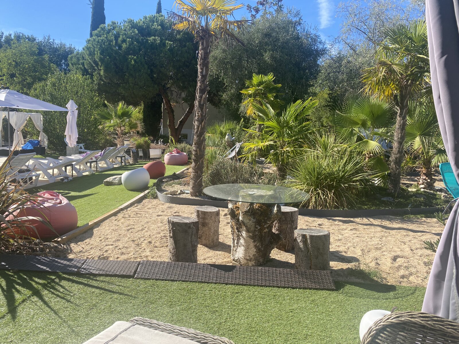 Garden with palm trees, a rustic log table and sun loungers.