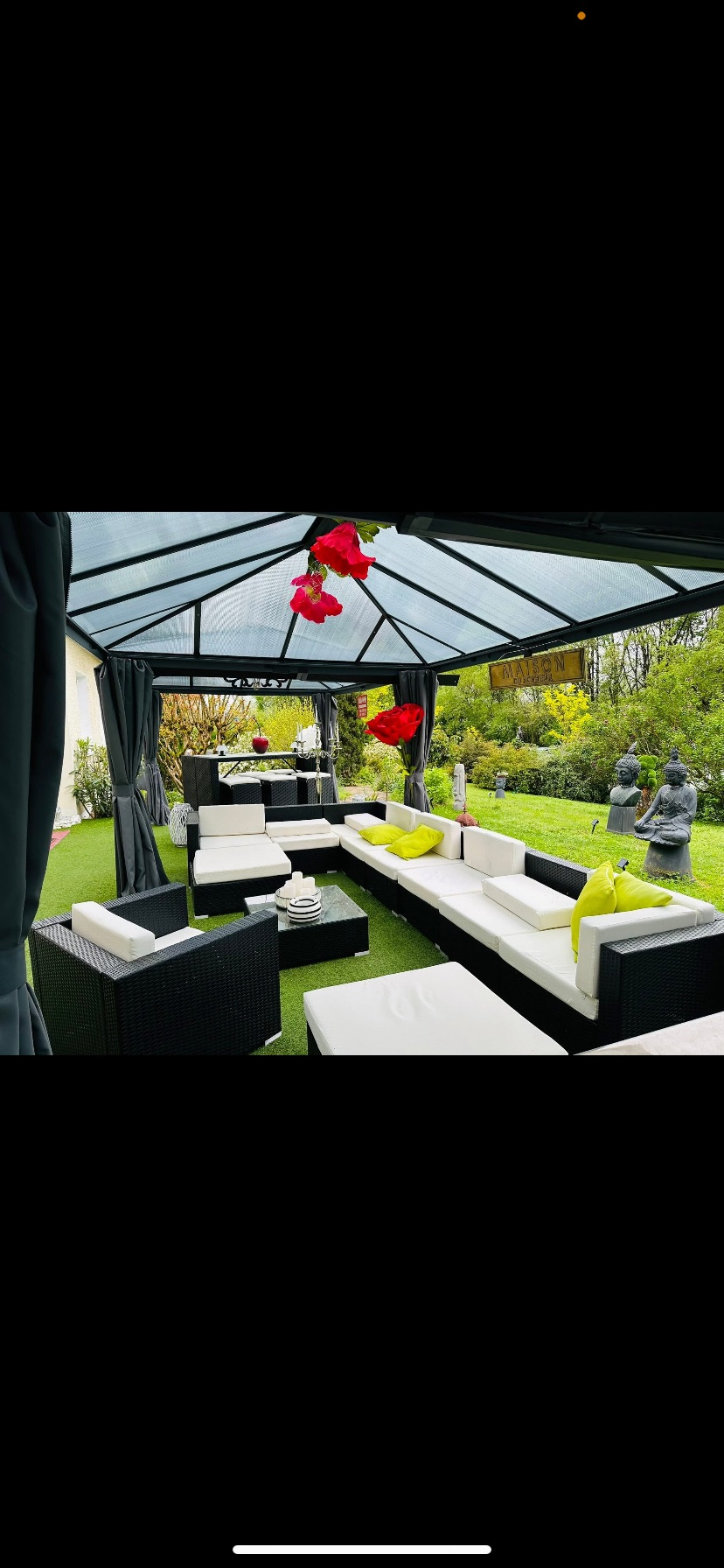 Covered outdoor lounge under a glass canopy, with black rattan sofas.