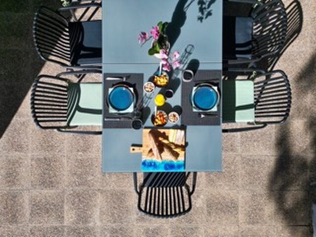 Overhead view of an outdoor table laid for breakfast with blue plates, a bread board and an orchid.