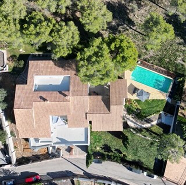 Aerial view of the house with its terracotta roof, the pool and the garden among the pines.