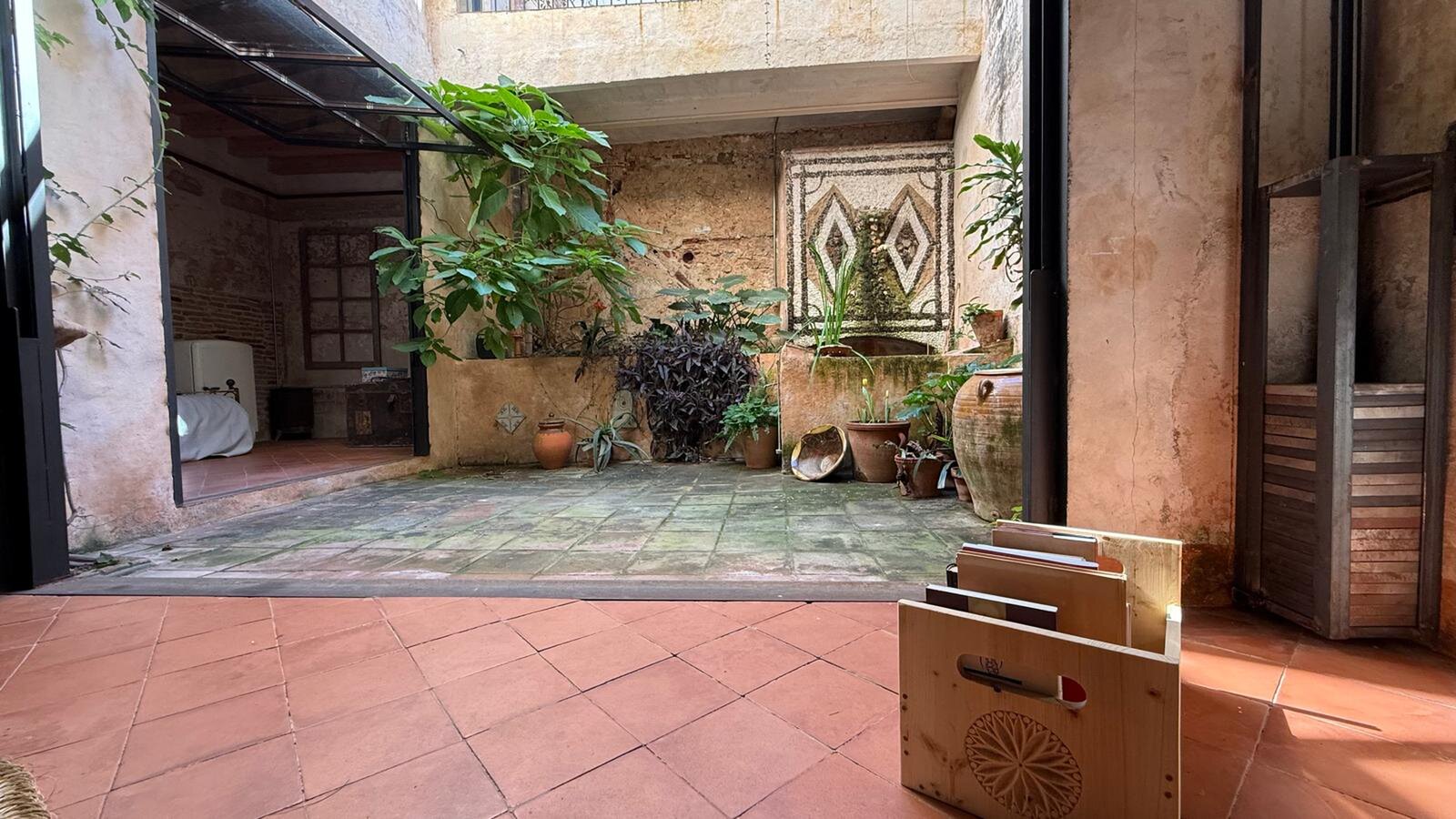 The view from a tiled room through open glass doors into the planted courtyard with its mosaic panel and clay pots.