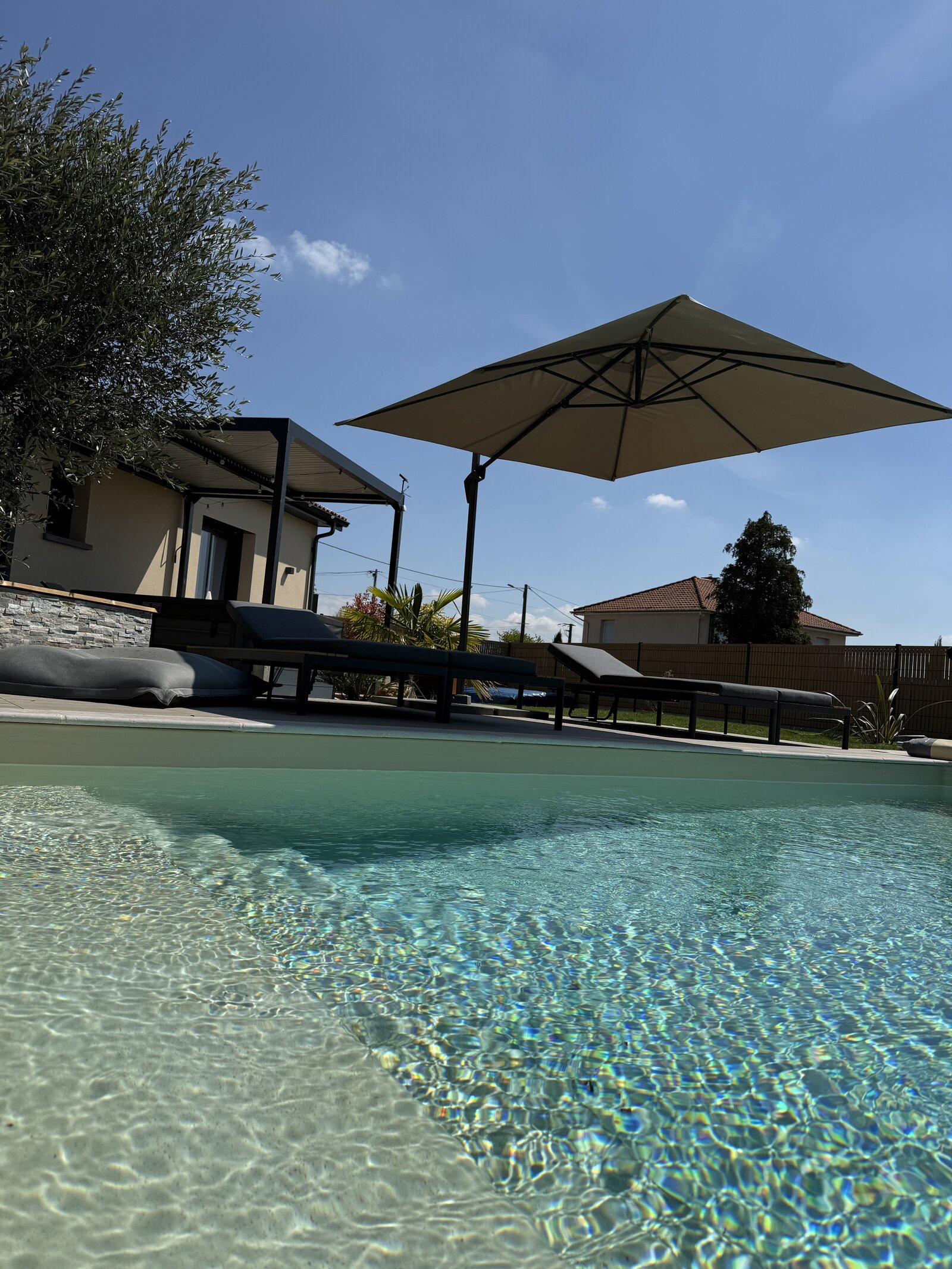 Poolside view across the water toward the loungers and umbrella.