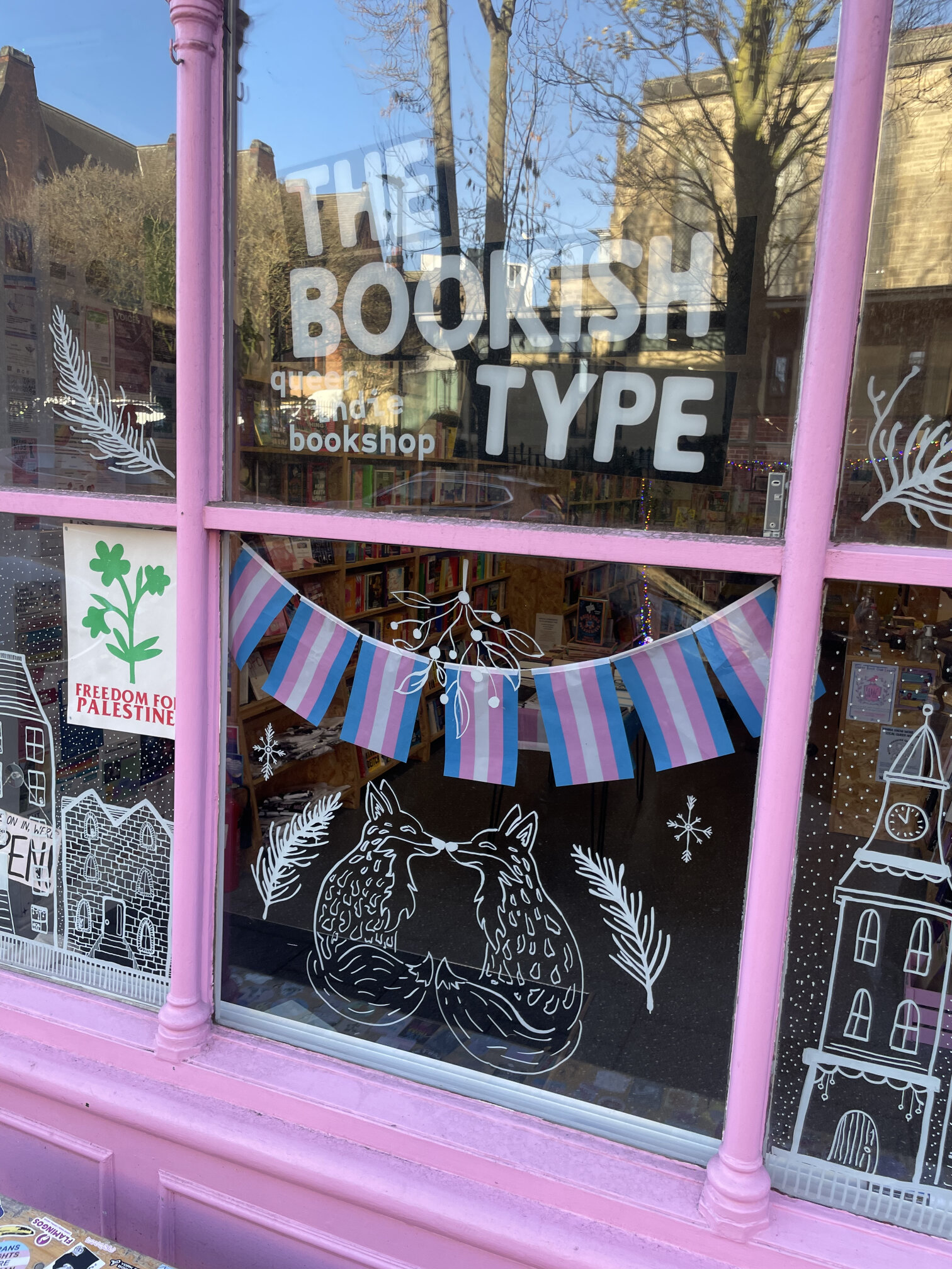 The shop window of The Bookish Type, painted pink, with trans pride bunting and two foxes drawn on the glass.