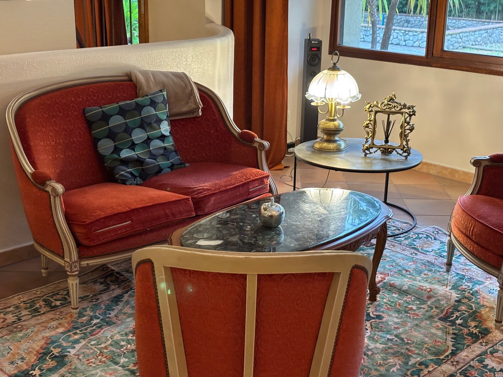 A settee in red velvet with a marble coffee table on an oriental rug, by the window to the garden.