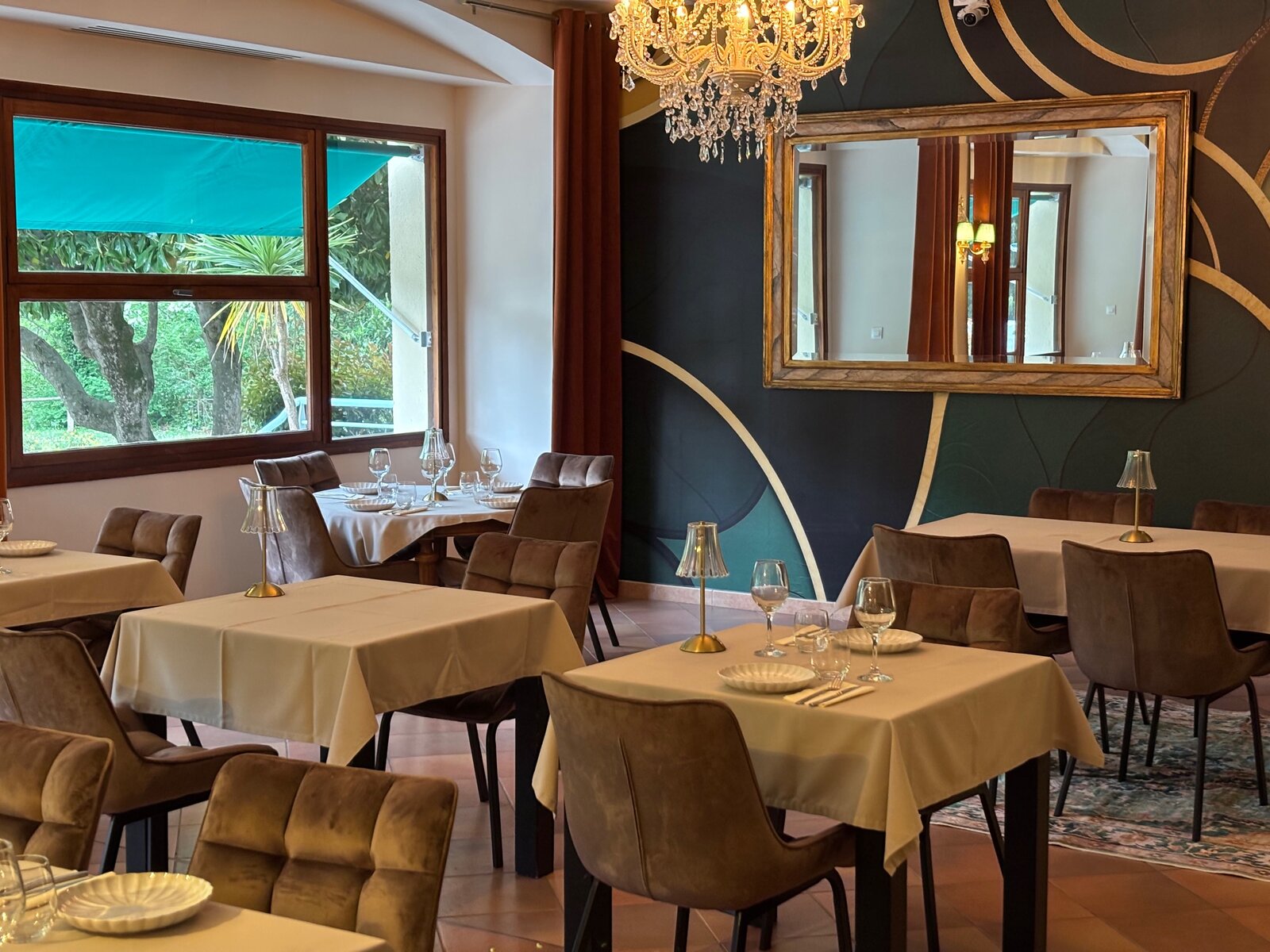 Laid tables in the restaurant, velvet chairs and a gilt mirror on a dark green wall.