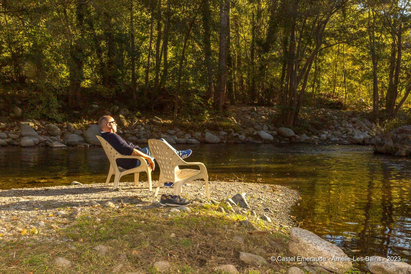A member of the family resting in a garden chair at the water, his shoes off beside him.