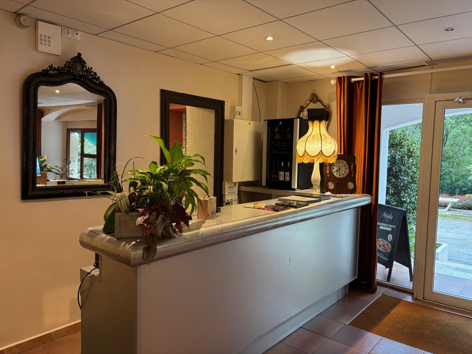 The reception desk by the entrance, with an old mantel clock, a fringed lamp and the door open to the garden.