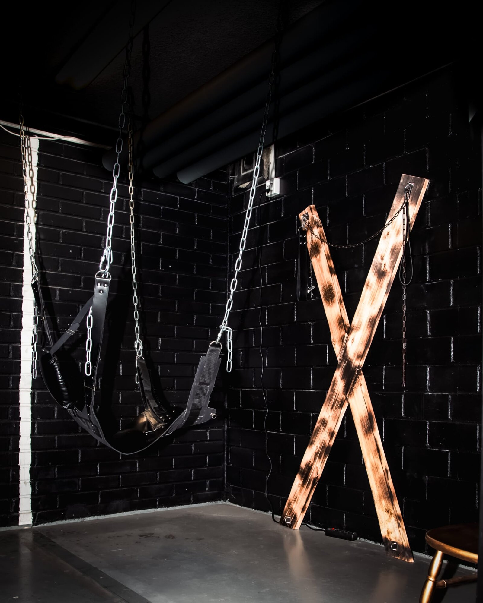 Dungeon corner with a sling and a wooden St Andrews cross on black brick walls