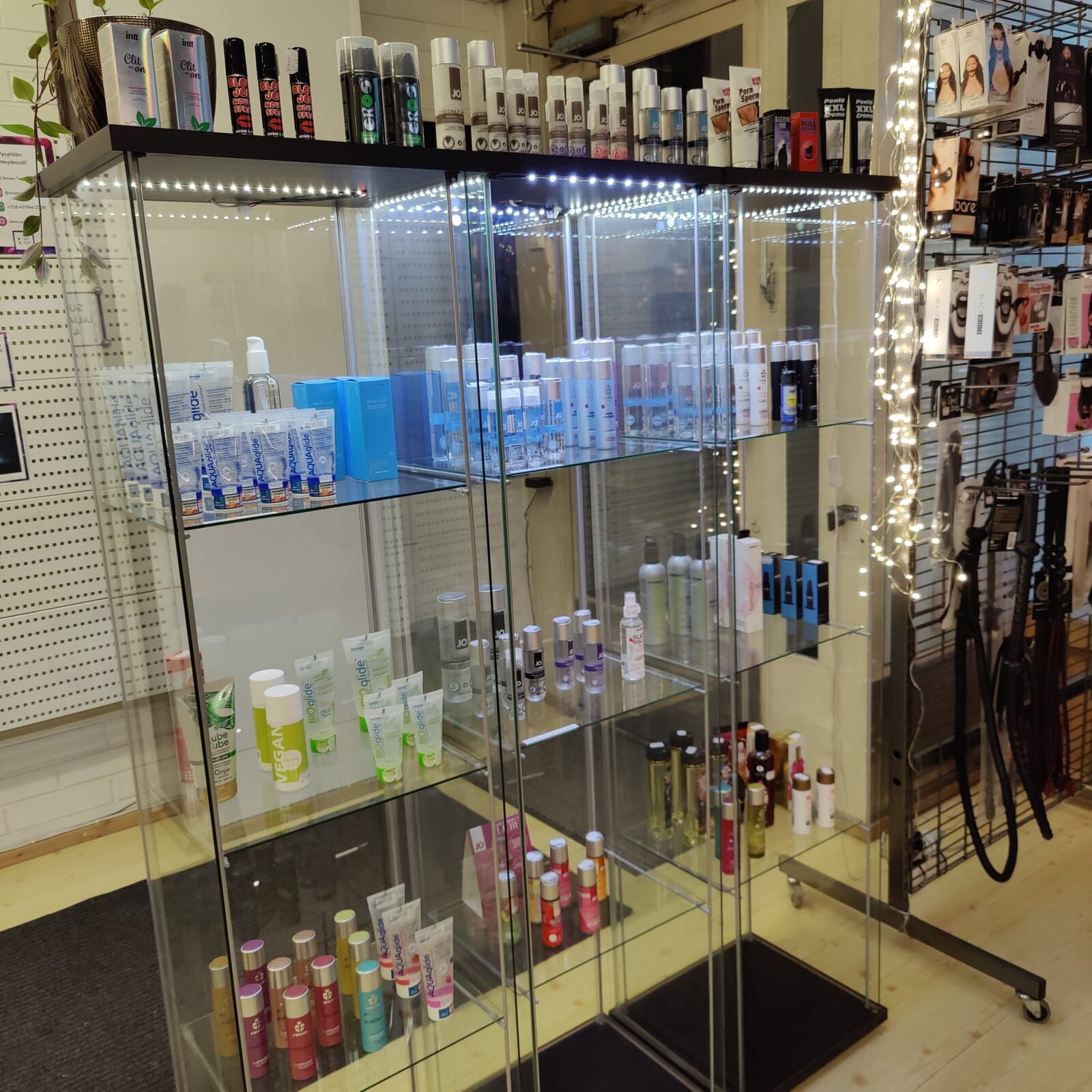 Glass cabinets with lubricants and massage oils, next to a rack of whips and gags