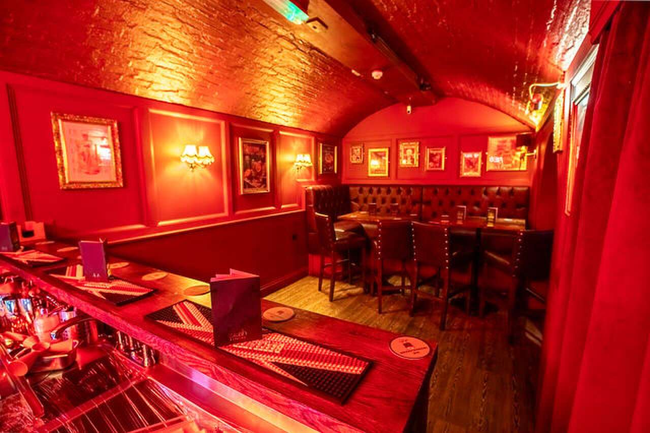 Leather booth seating and framed pictures along the red walls of the Negroni Lounge.