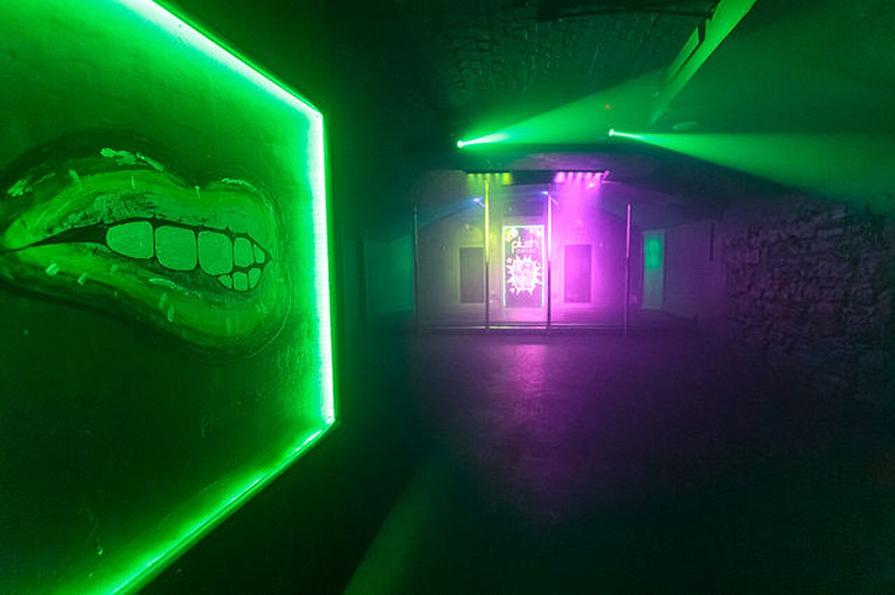 Green lasers over the dance floor, beside a neon-framed painting of a pair of lips.
