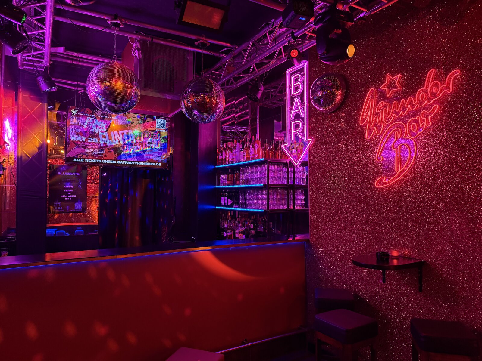 The back bar with the WunderBar neon sign on the glitter wall and a lit BAR arrow beside the shelves