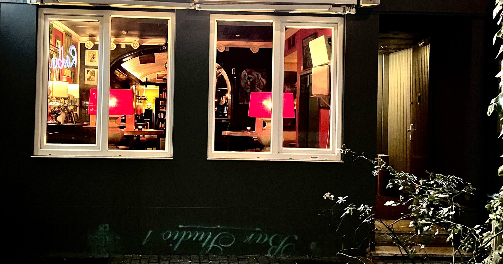 The bar's illuminated front windows and entrance door, seen reflected from across the street.