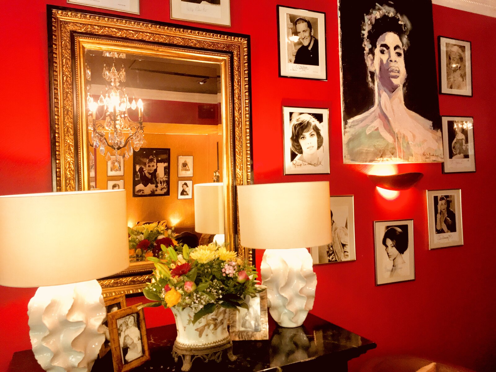 A close-up of the red wall's portrait gallery, with a gilt mirror, fresh flowers and a painted portrait of Prince.