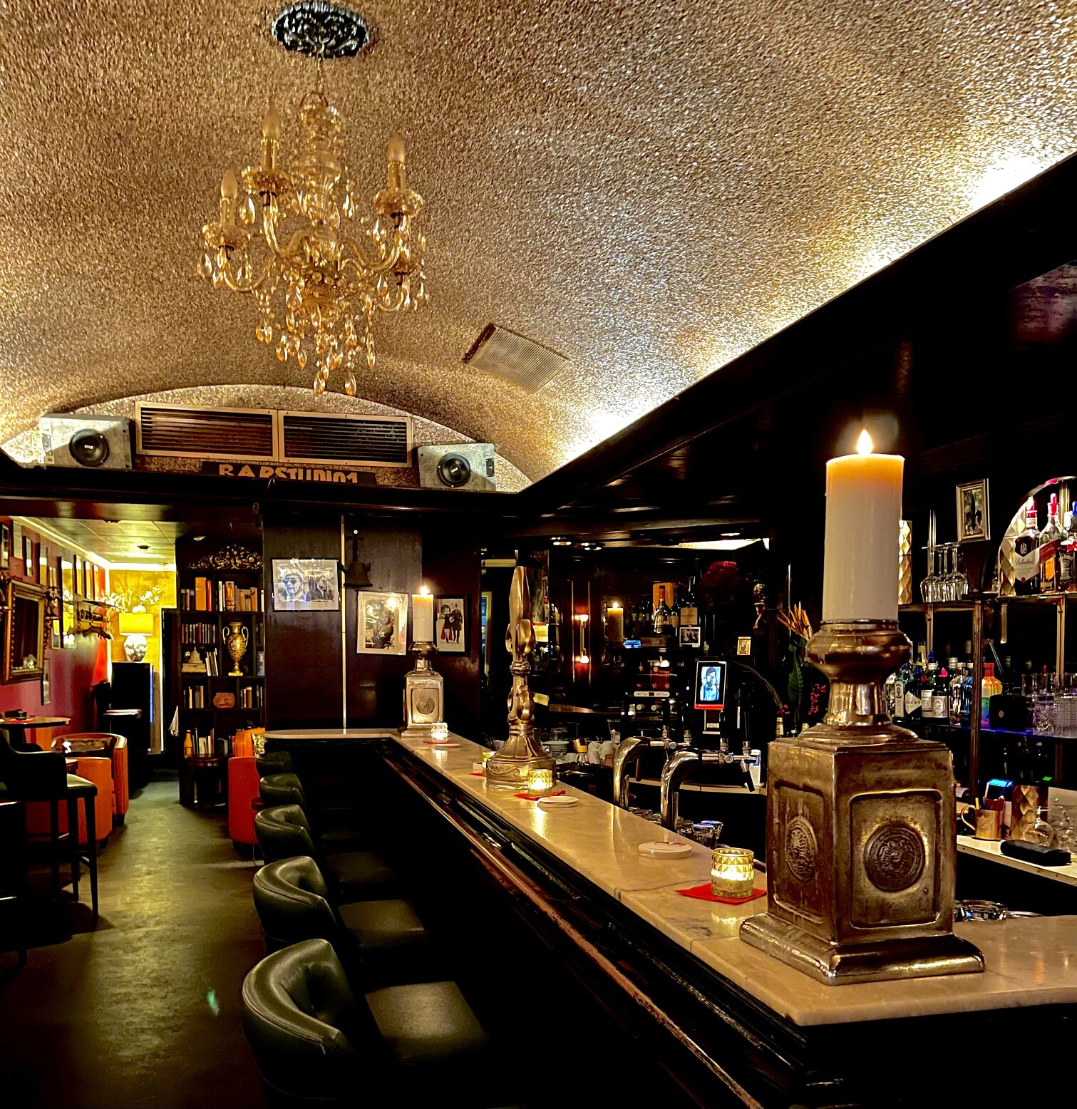 The long bar counter with its marble top, beer taps and rows of spirits, lit by a chandelier.