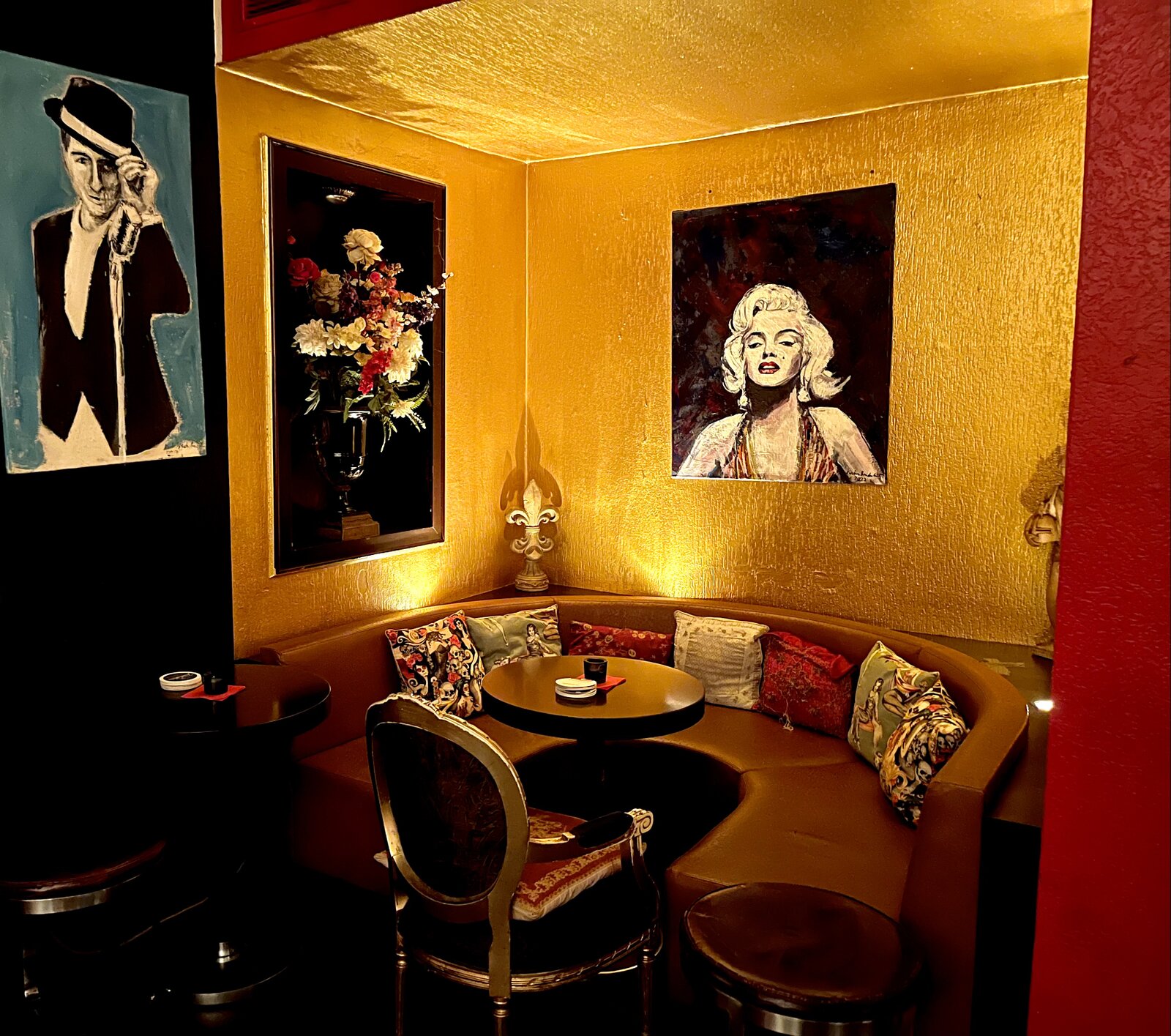 A round corner booth beneath gold-painted walls, flanked by paintings of Marilyn Monroe and Frank Sinatra.