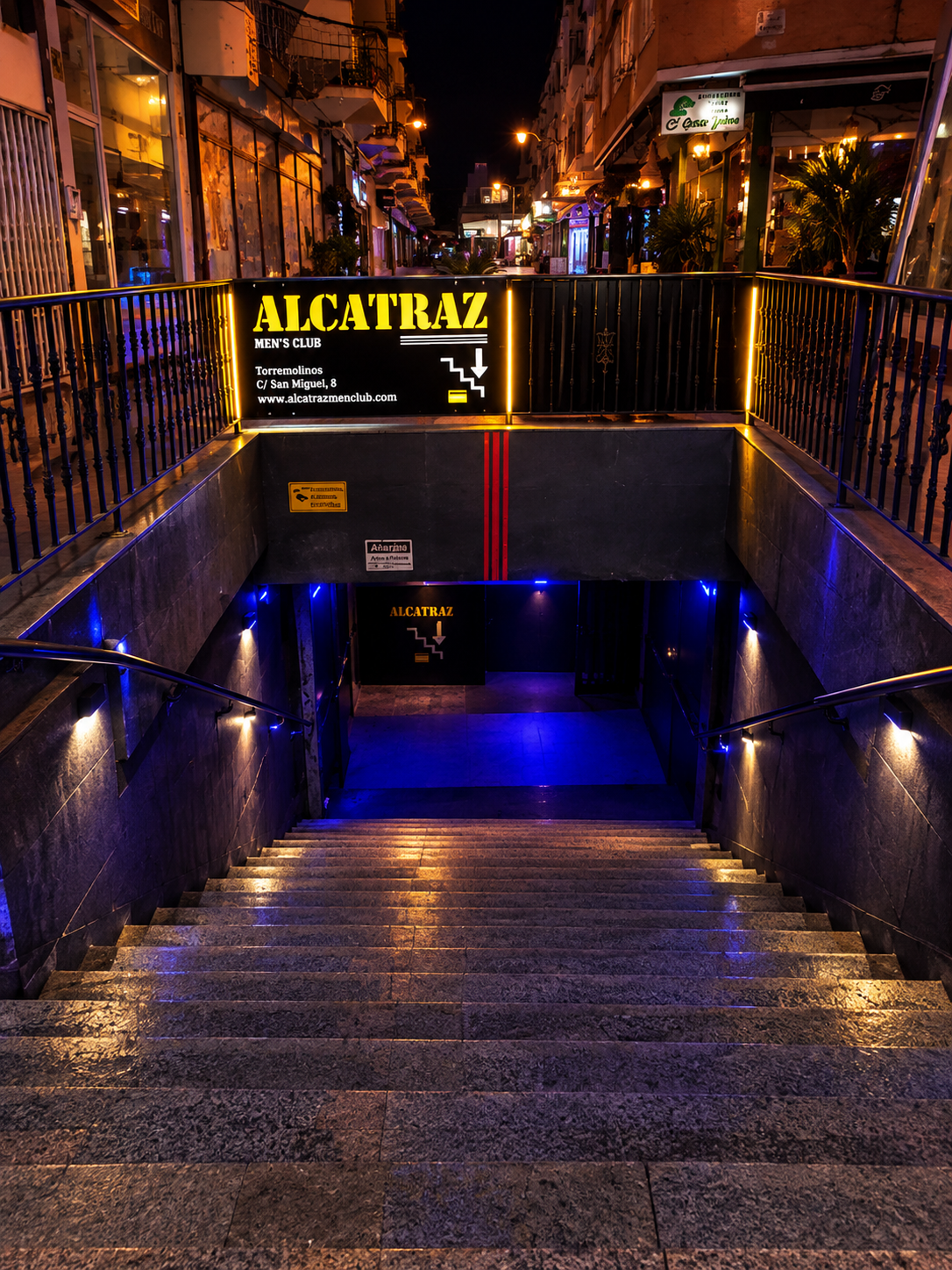 Stairs down from Calle San Miguel to the entrance, under the lit Alcatraz Men's Club sign.