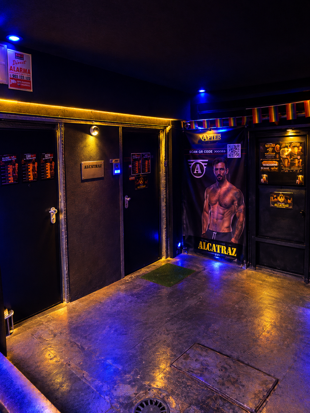 The lobby at the foot of the stairs, with the doors to the club on the left and rainbow bunting over an Alcatraz After banner.