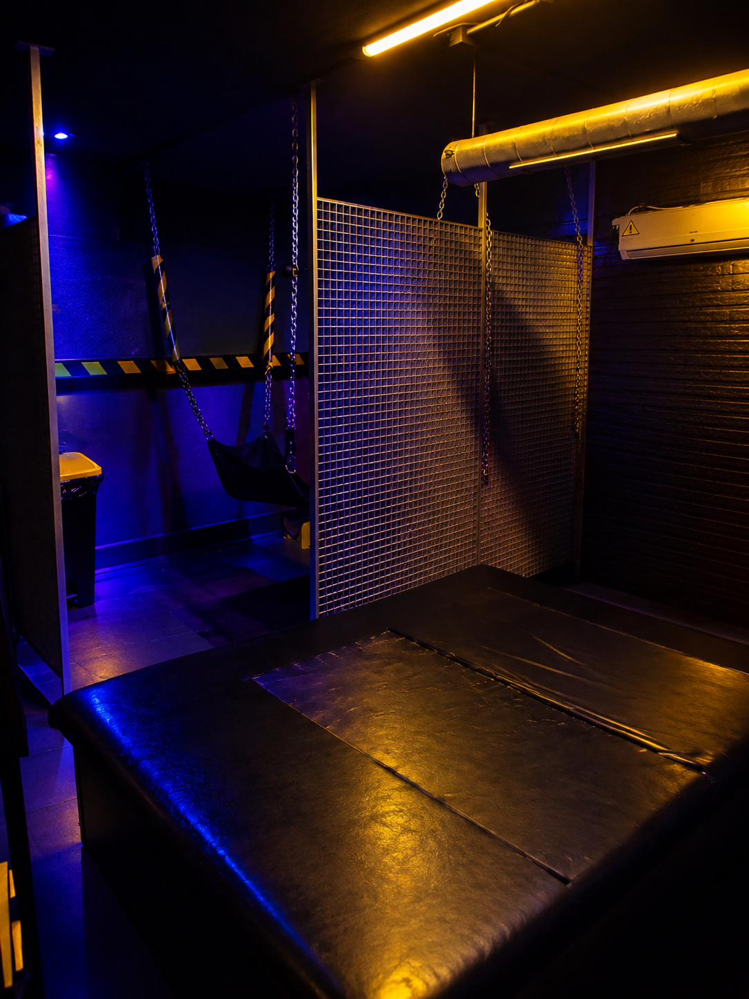 Play area with a large padded platform, chains hanging from the ceiling and a sling behind a grated partition.